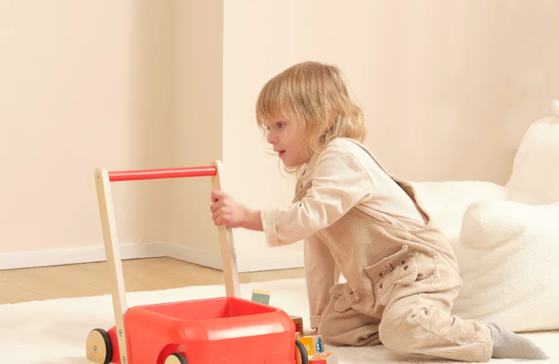 A toddler pushing a wooden walker across a sunlit room